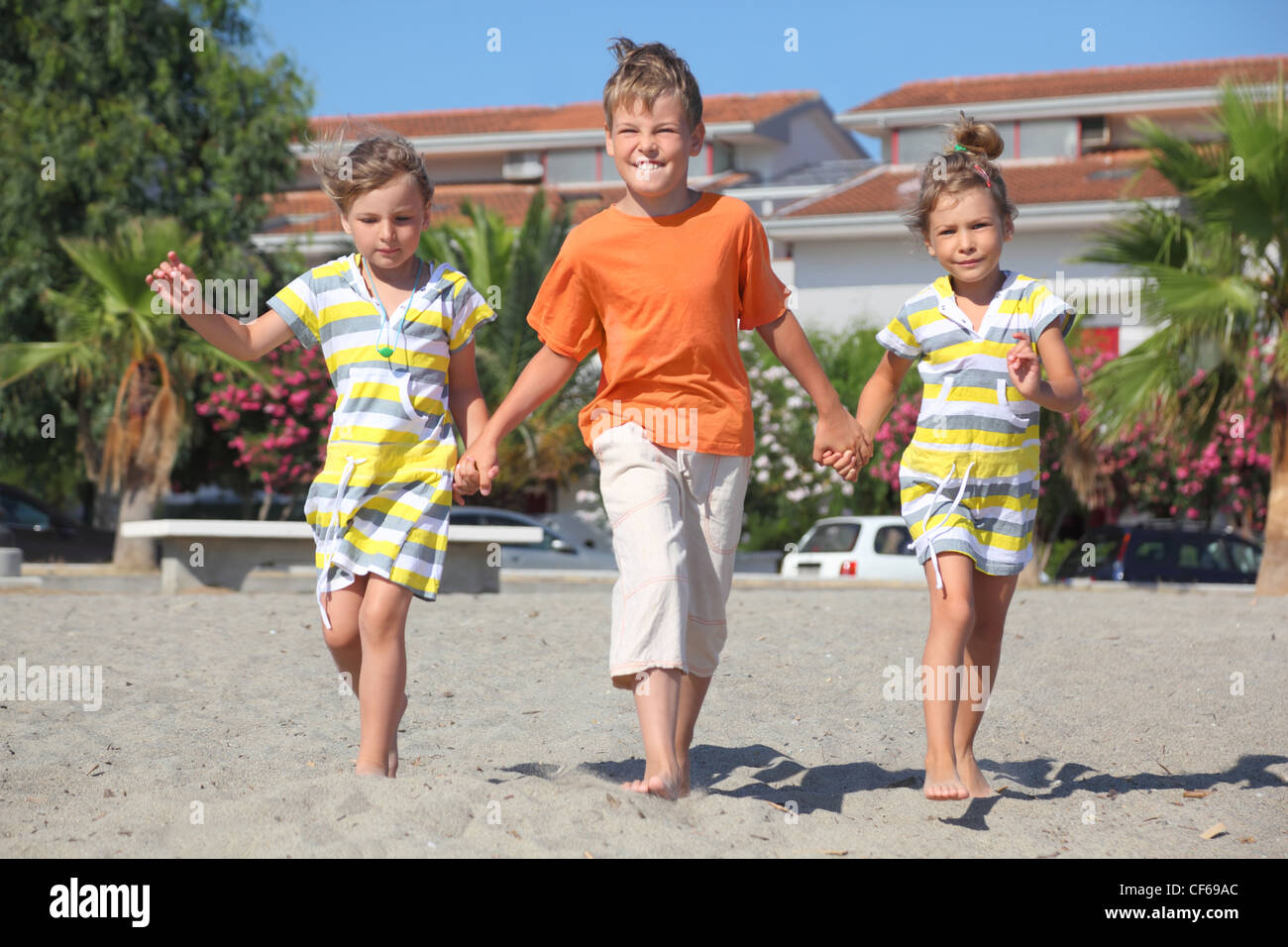 little boy and two girls walking on beach, holding for hands, palms and building Stock Photo