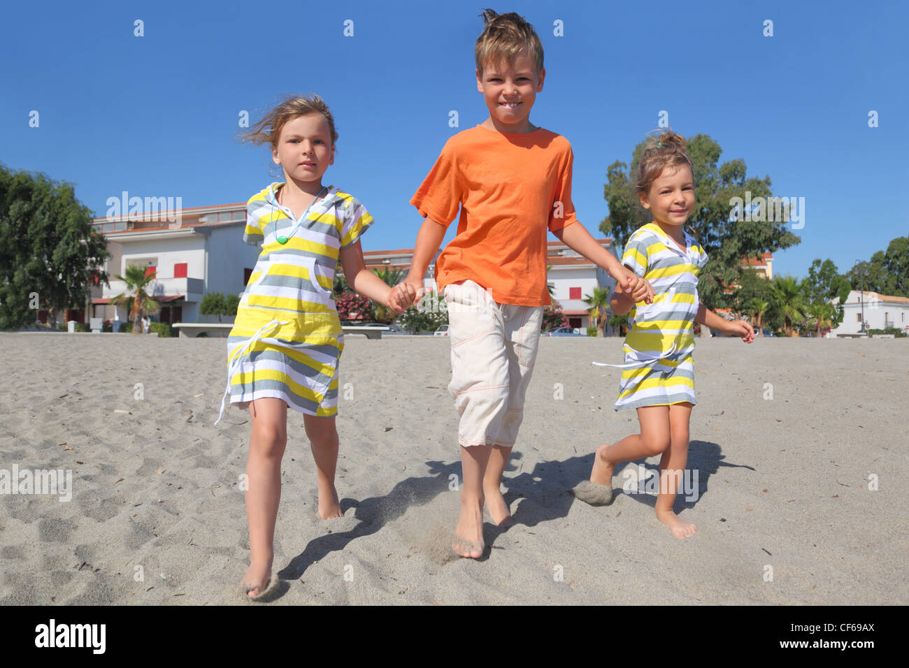 little boy and two girls walking on beach, holding for hands, trees and building Stock Photo