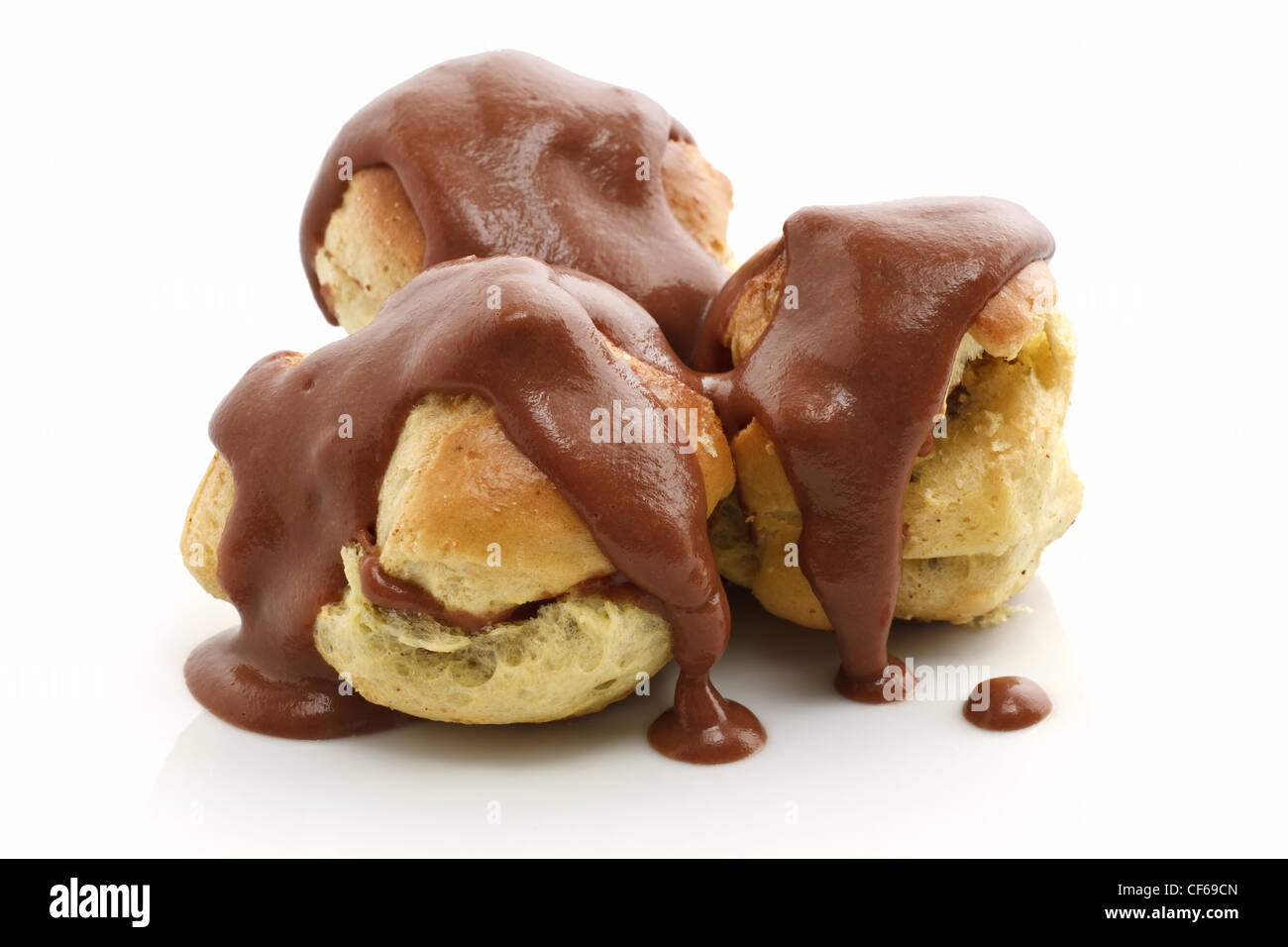 three profiteroles with chocolate sauce over white background Stock