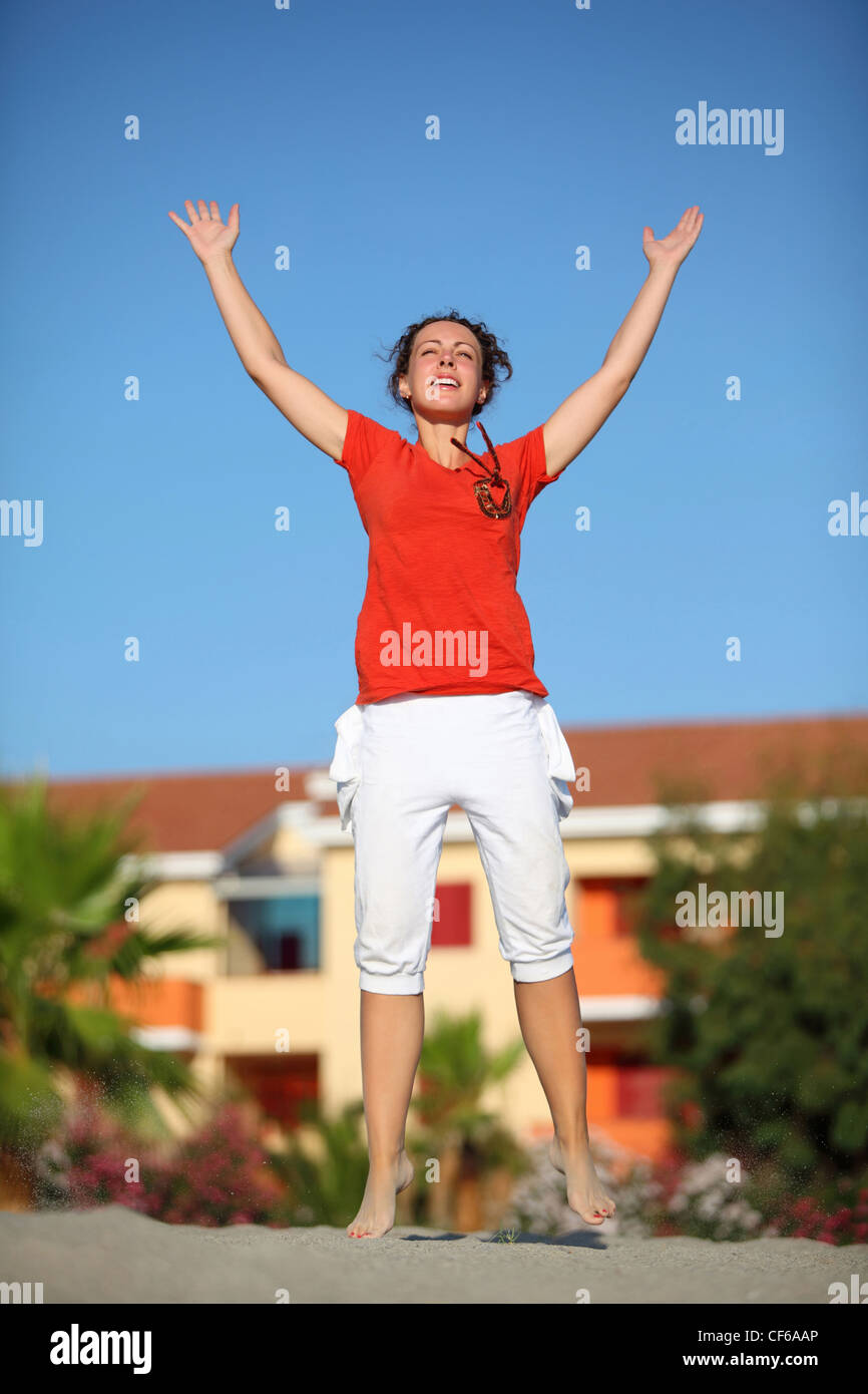 Woman jumps on  beach and lifts hands and head to sky Stock Photo