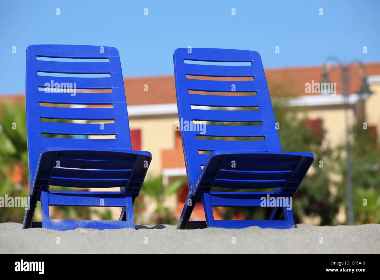 Two empty dark blue chairs stand on sand under  sun Stock Photo