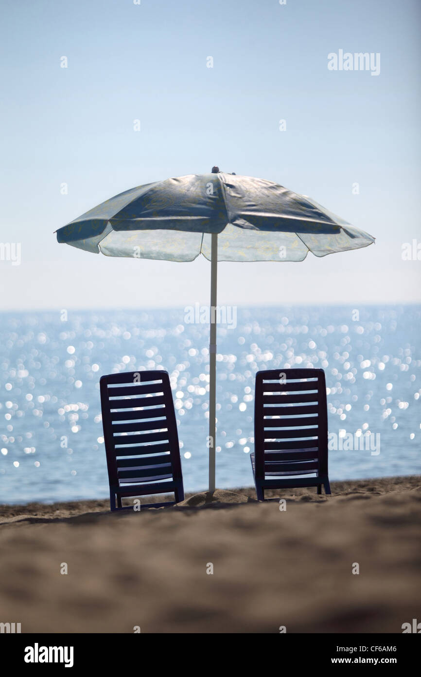 Near  sea ashore two dark blue plastic chairs stay under  large umbrella Stock Photo