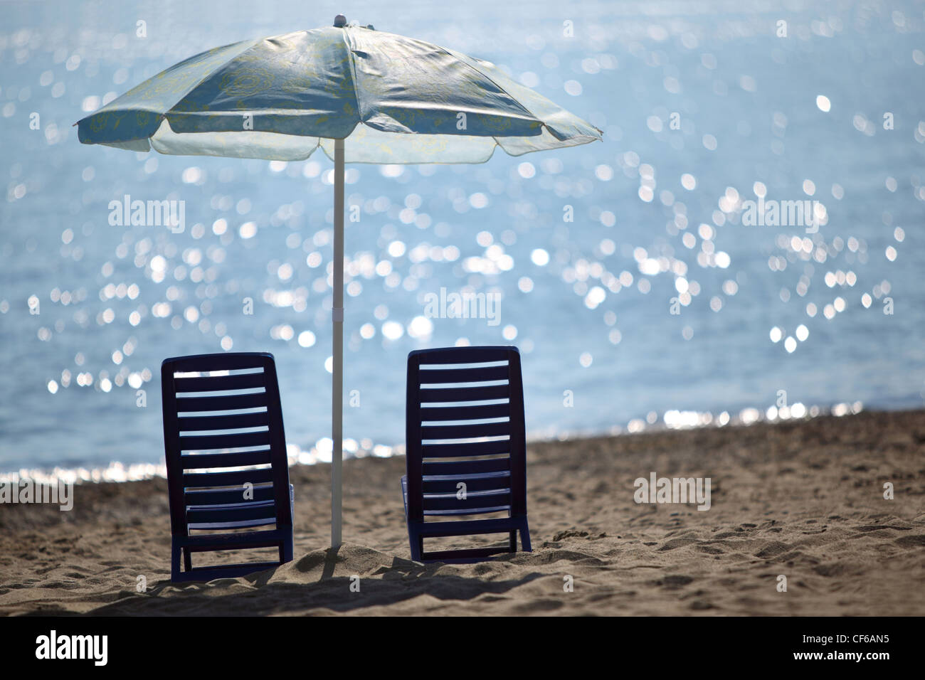 Two dark blue empty chairs  stand on  beach near  sea under shade of large umbrella Stock Photo