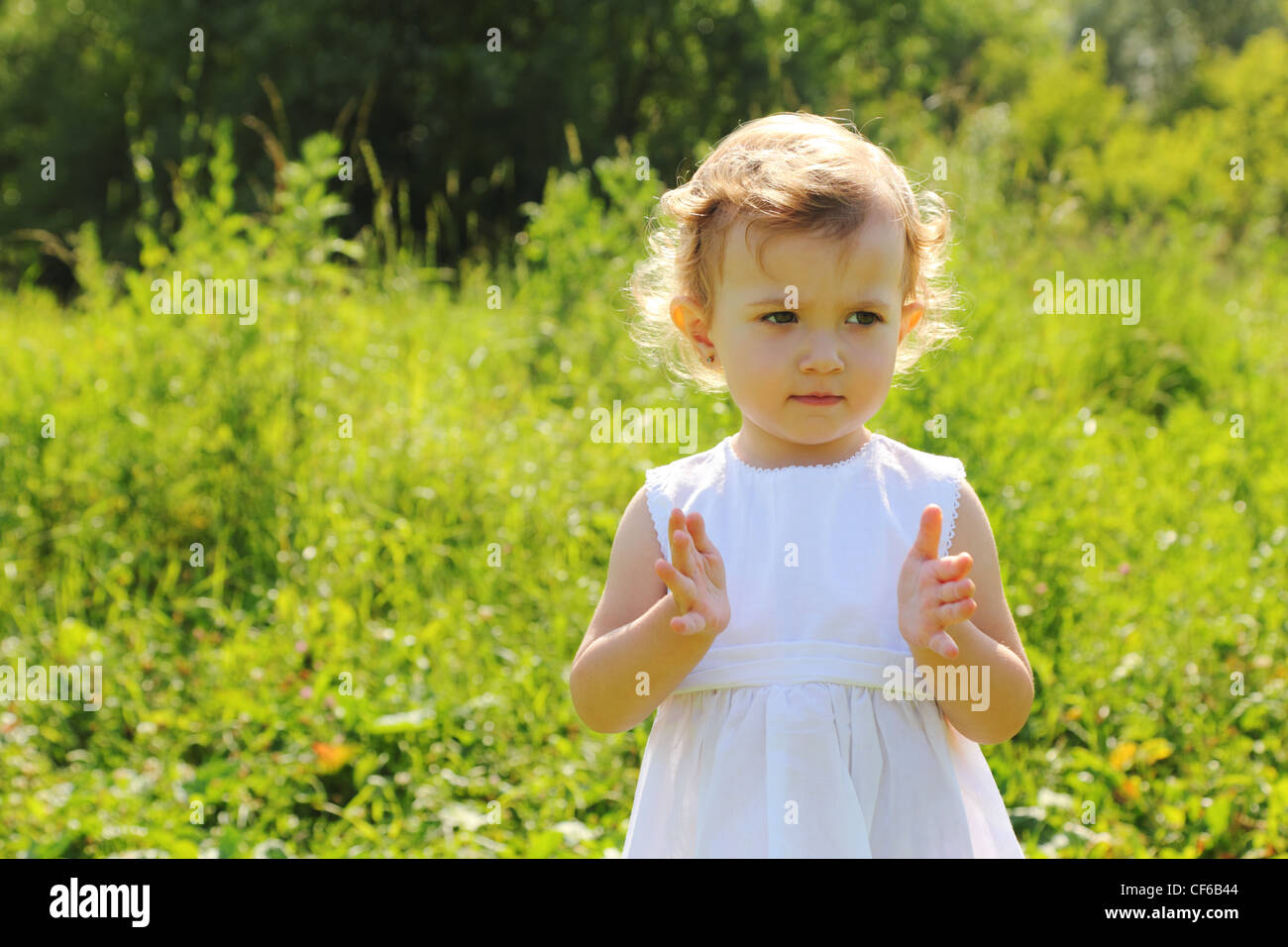 Little girl standing in the grass shows something with her hands Stock ...