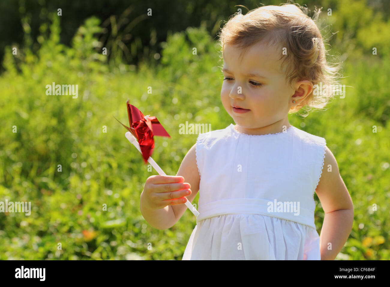 Little girl with the red pinwheel standing in the grass and looking at the pinwheel Stock Photo
