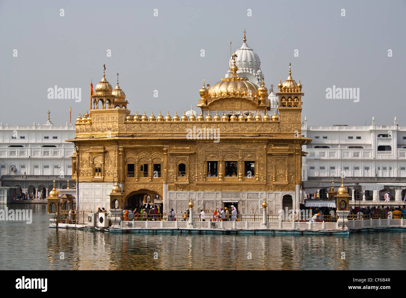 Darbar Sahib and Amrit Sarovar inside Golden Temple with devotees (men and women) on the causeway over the water body Stock Photo