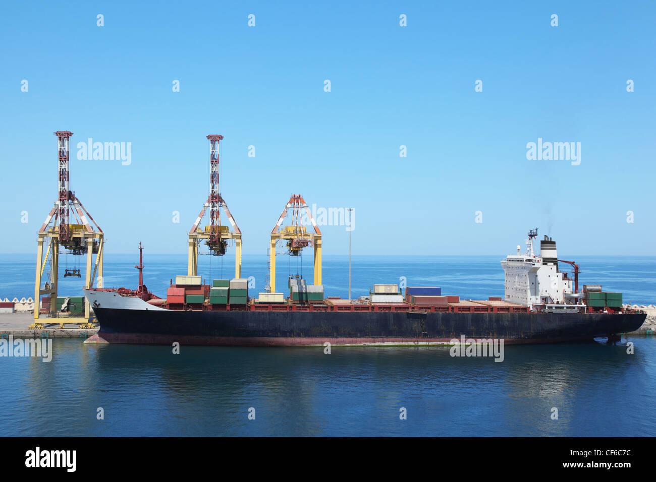 big merchant ship with cargos on a board at its moorings in port. Stock Photo