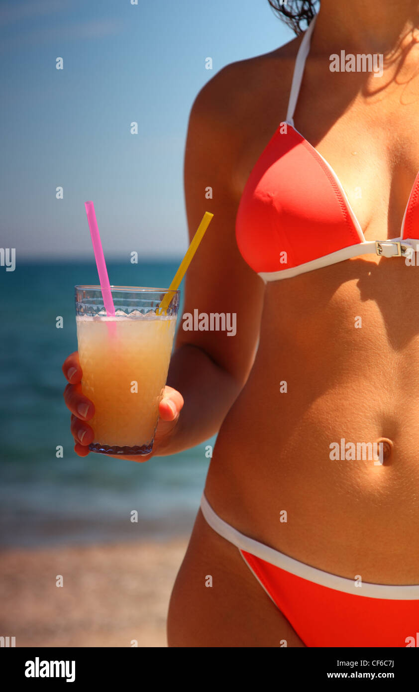 Body of girl in red swimsuit. She holds a glass of juice with two tubes. Stock Photo