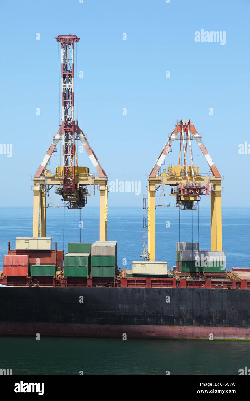 big merchant ship with many big cargos on a board in port. Stock Photo