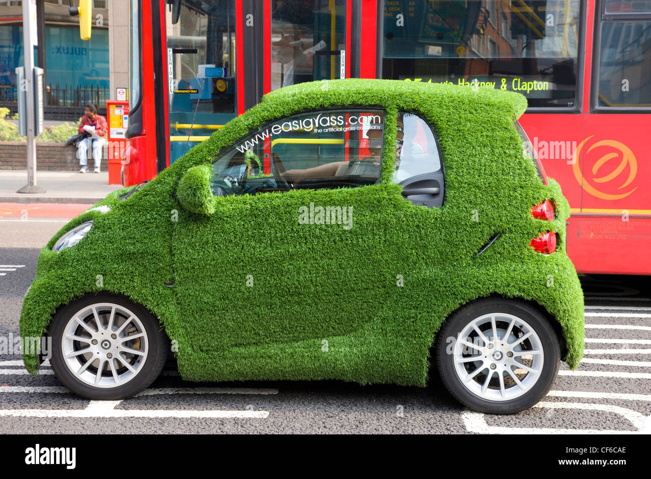 A promotional electric car covered in fake grass at traffic lights in Aldgate. Stock Photo