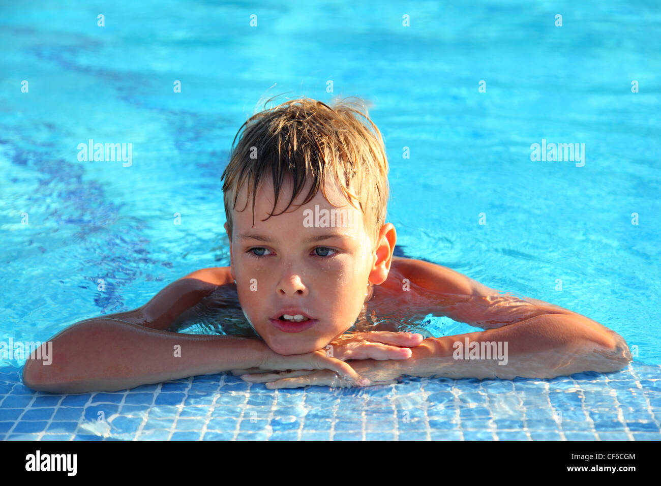 Little boy lies in swimming-pool and thoughtfully looks sideways Stock Photo