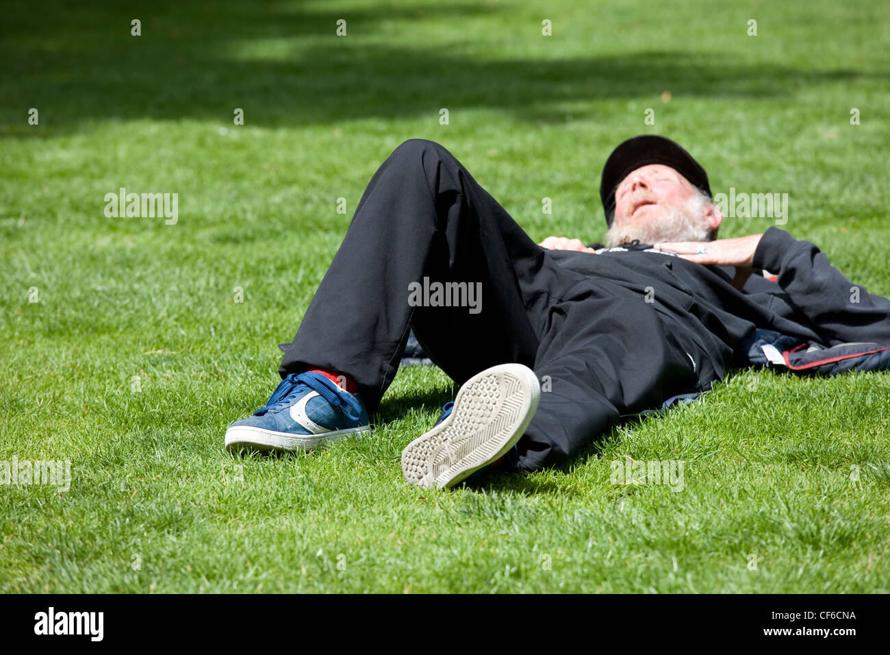 An elderly gentleman asleep on the grass in a London park. Stock Photo