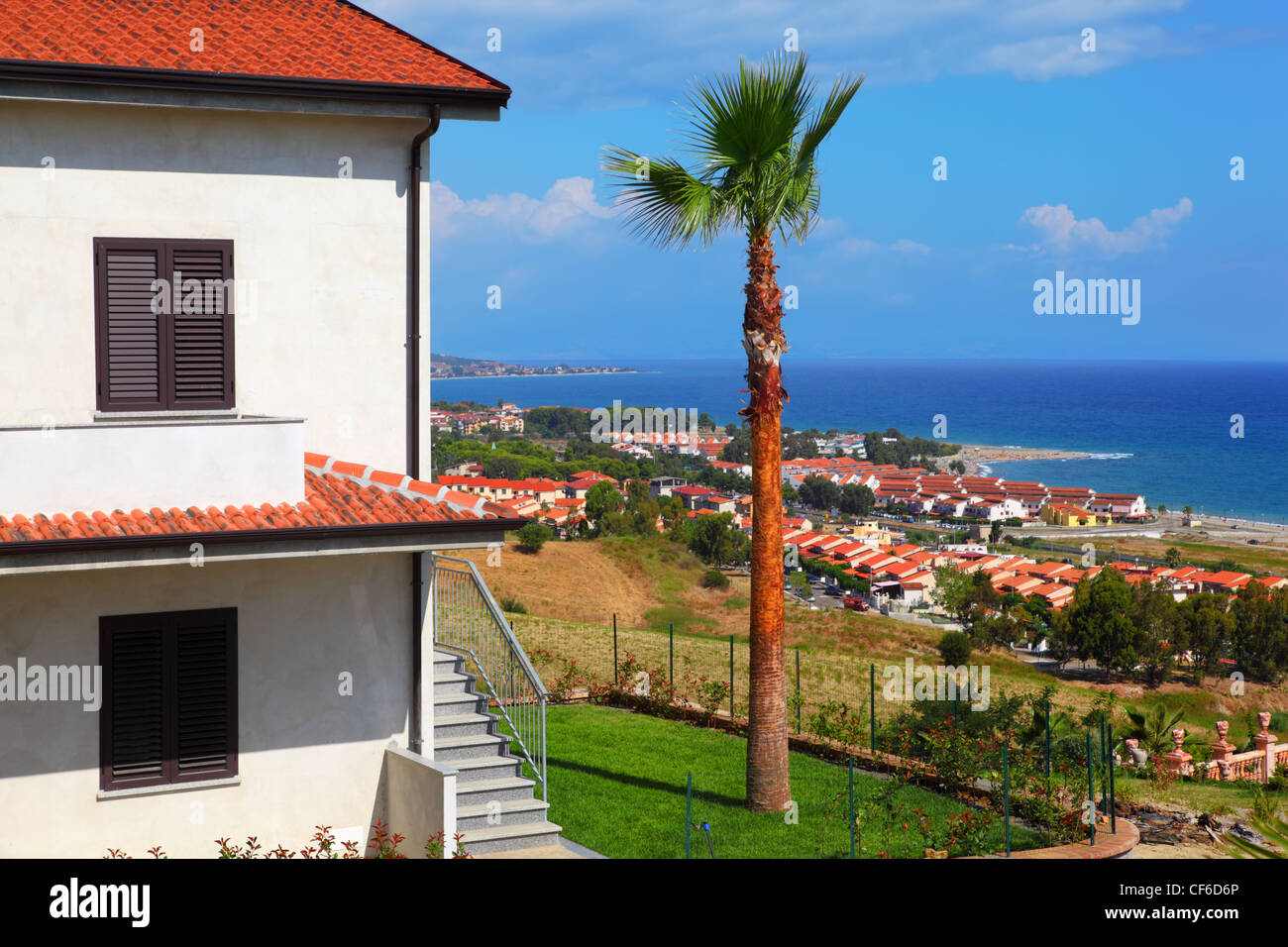 Big white two-story house with brown roof, palm trees and stairs on coast at city Stock Photo