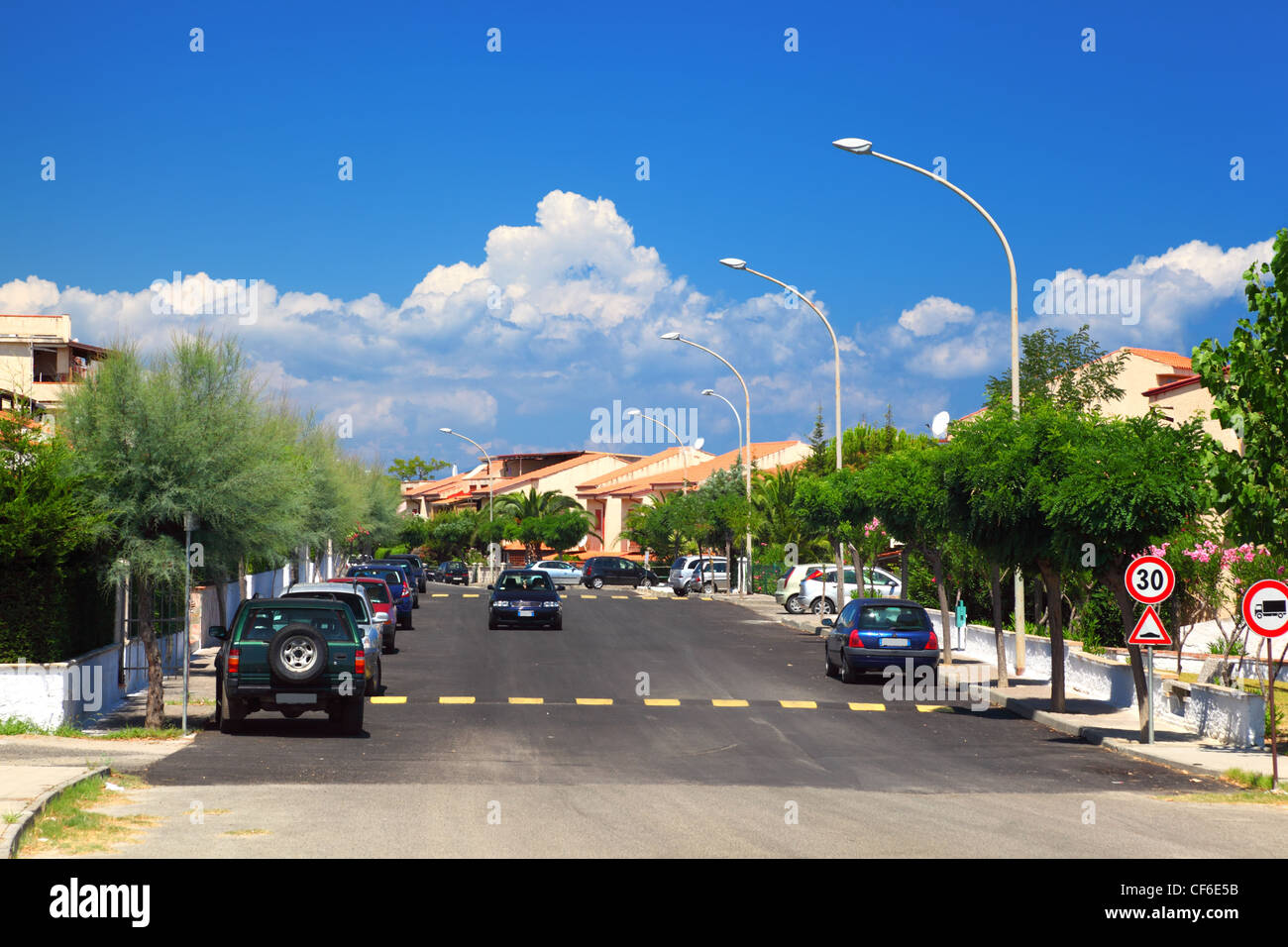 Cars drive on road and on the sidewalks are palm trees in residential area. Stock Photo