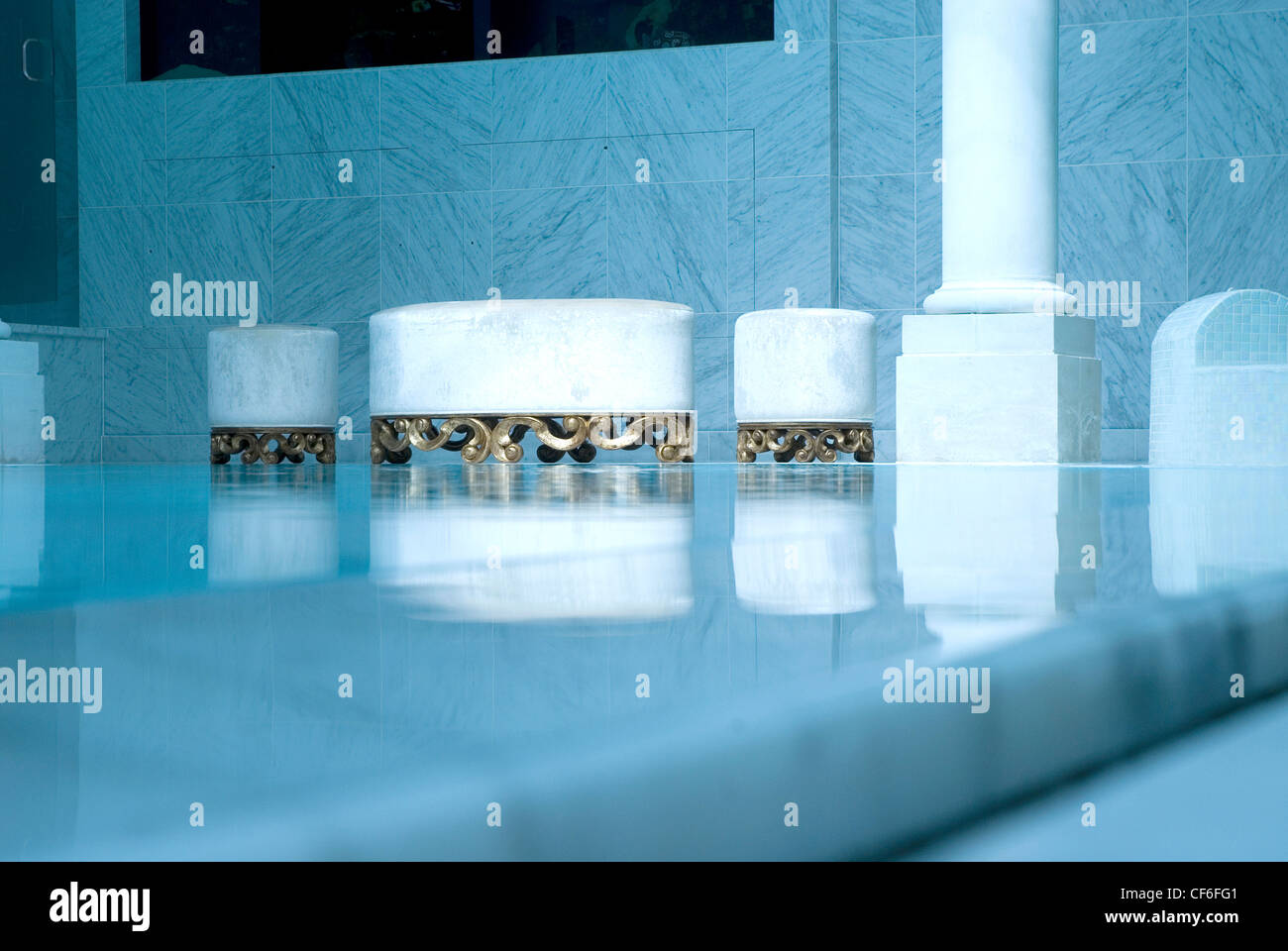 The interior of a high end private pool, an oblique angle to the water surface with reflections and white/gold cushion stools. Stock Photo