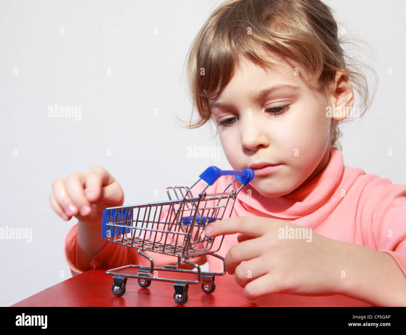 Cute little blond girl care play with empty toy shopping trolley Stock Photo