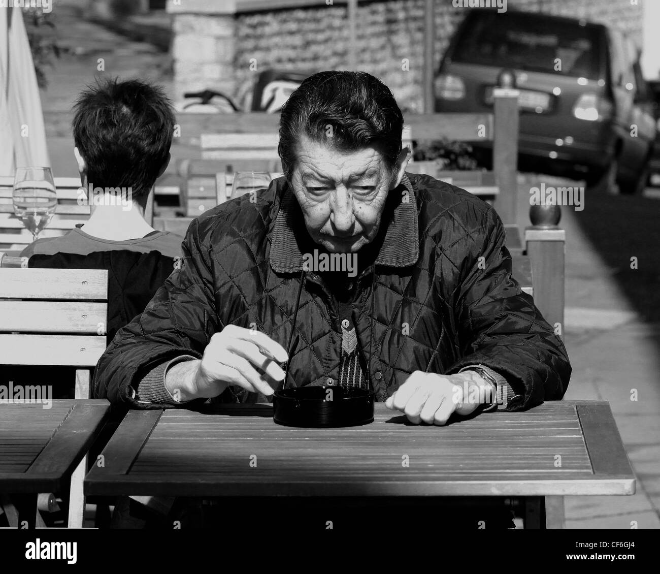 An Italian senior citizen sitting and smoking on a table outside a local wine bar. Spilimbergo, Italy. Stock Photo