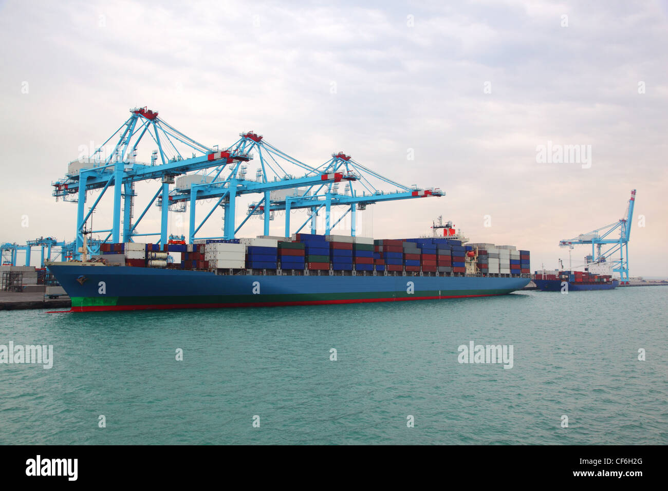 Big cargo boat and small barge docked to industrial port with blue ...