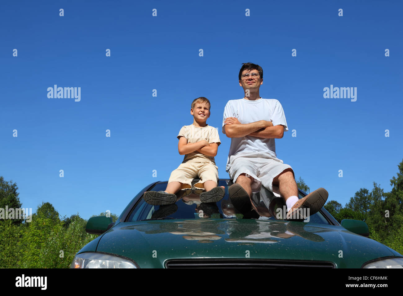 Father with  son of sit on   roof of car in   day and peep in  distance, laying down hands on  breast Stock Photo