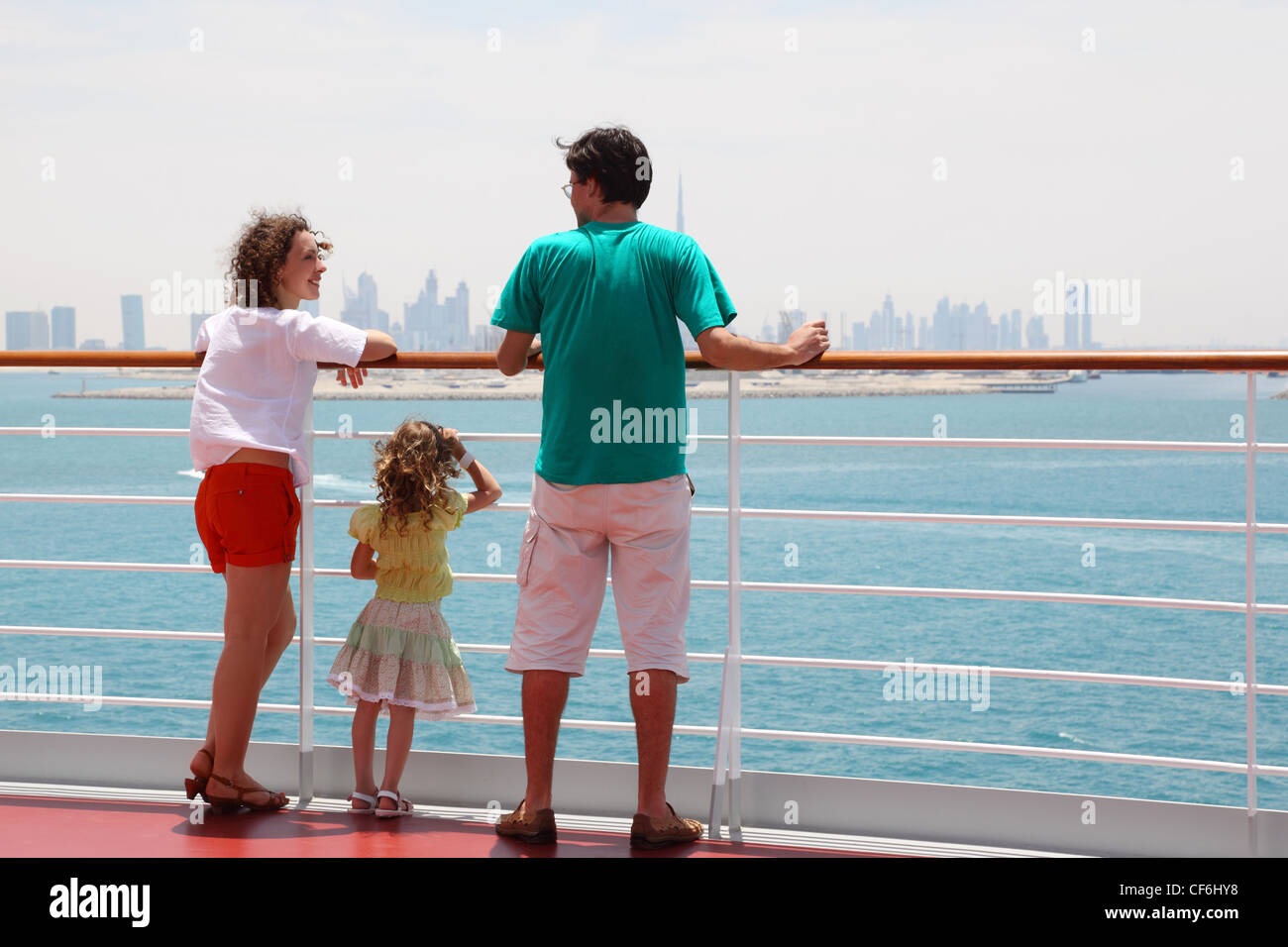 family with daughter standing on cruise liner deck, view from back, city on horizon Stock Photo