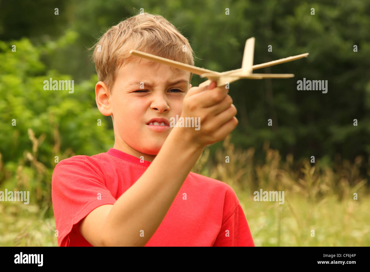 little boy in red T-shirt plays with wooden airplane on nature Stock Photo