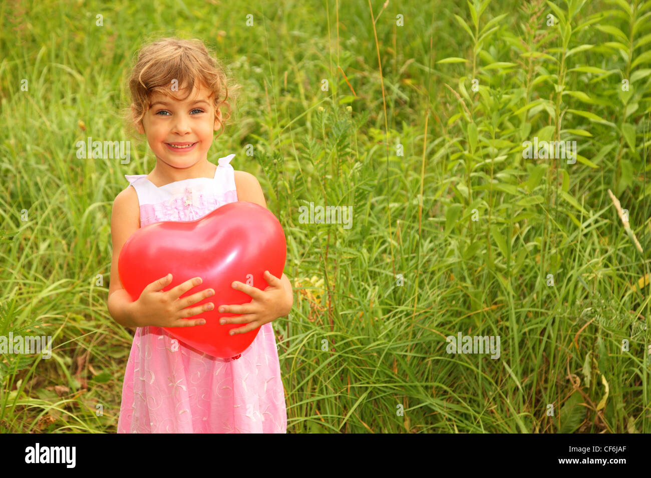 beautiful little girl in pink dress holding red balloon. Girl on nature Stock Photo