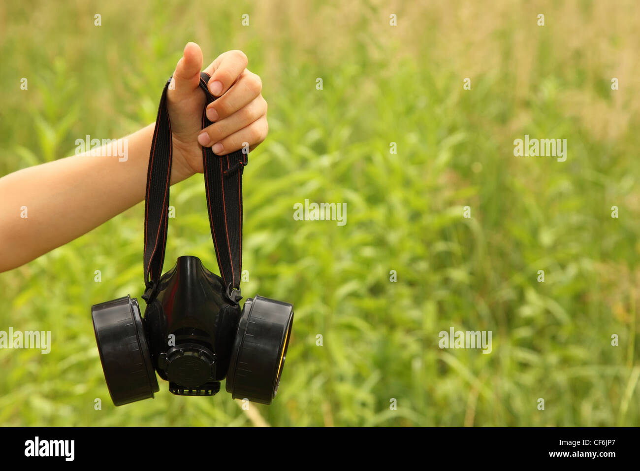 Children's hand holding big black respirator on background of green grass Stock Photo