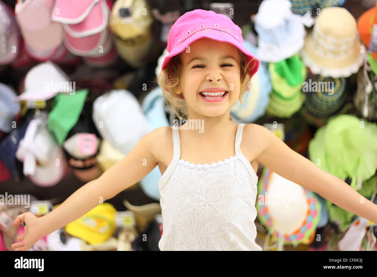 portrait of little girl trying pink panama in store and smiling, counter with commodity Stock Photo