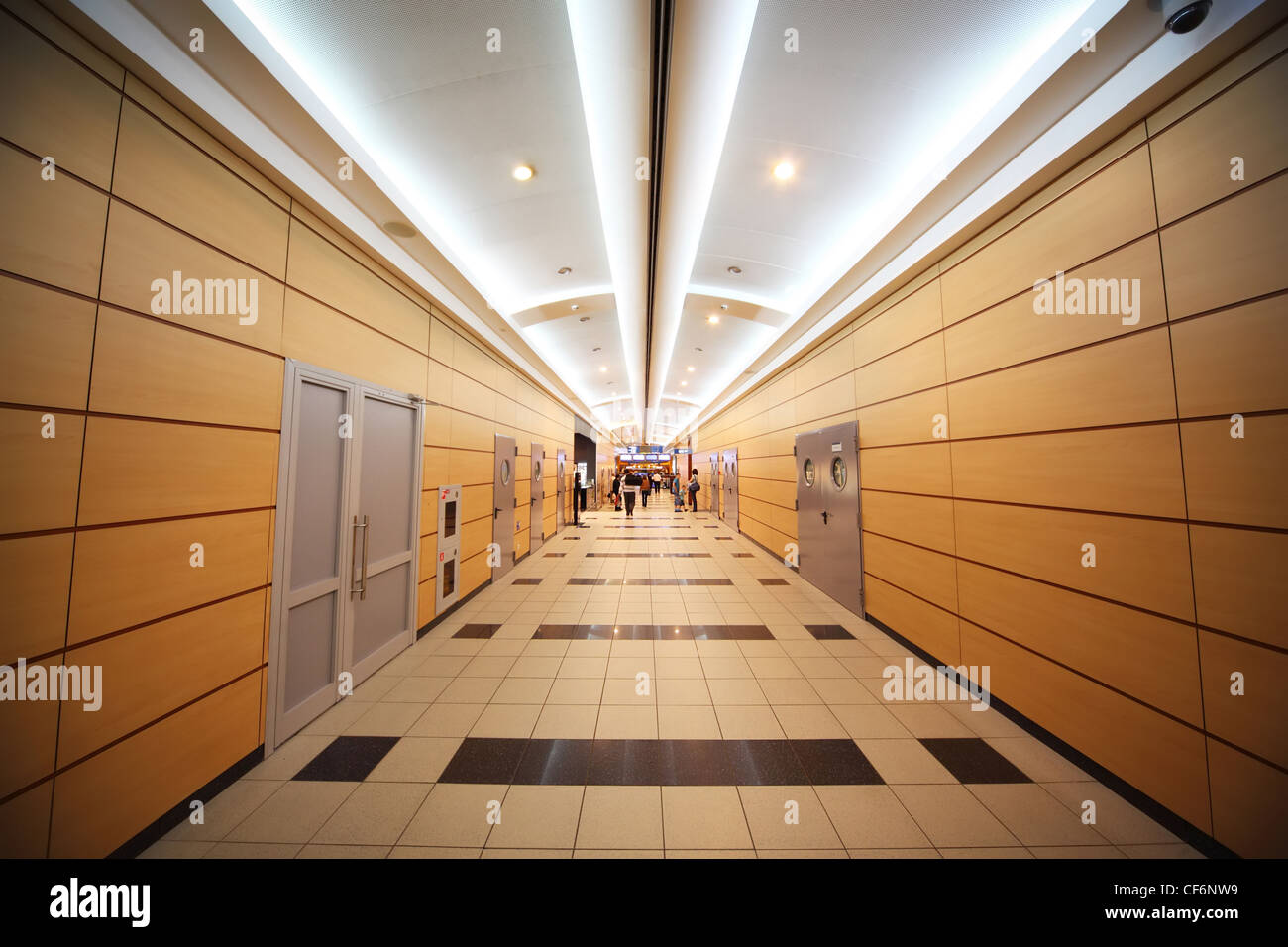 People go through a long, orange, light corridor in airport. Modern interior. Stock Photo