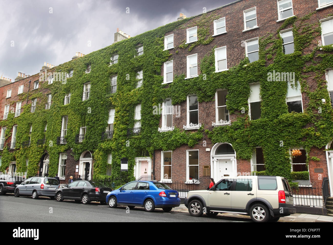 several cars parked near the four-storey building of red brick with ivy Stock Photo