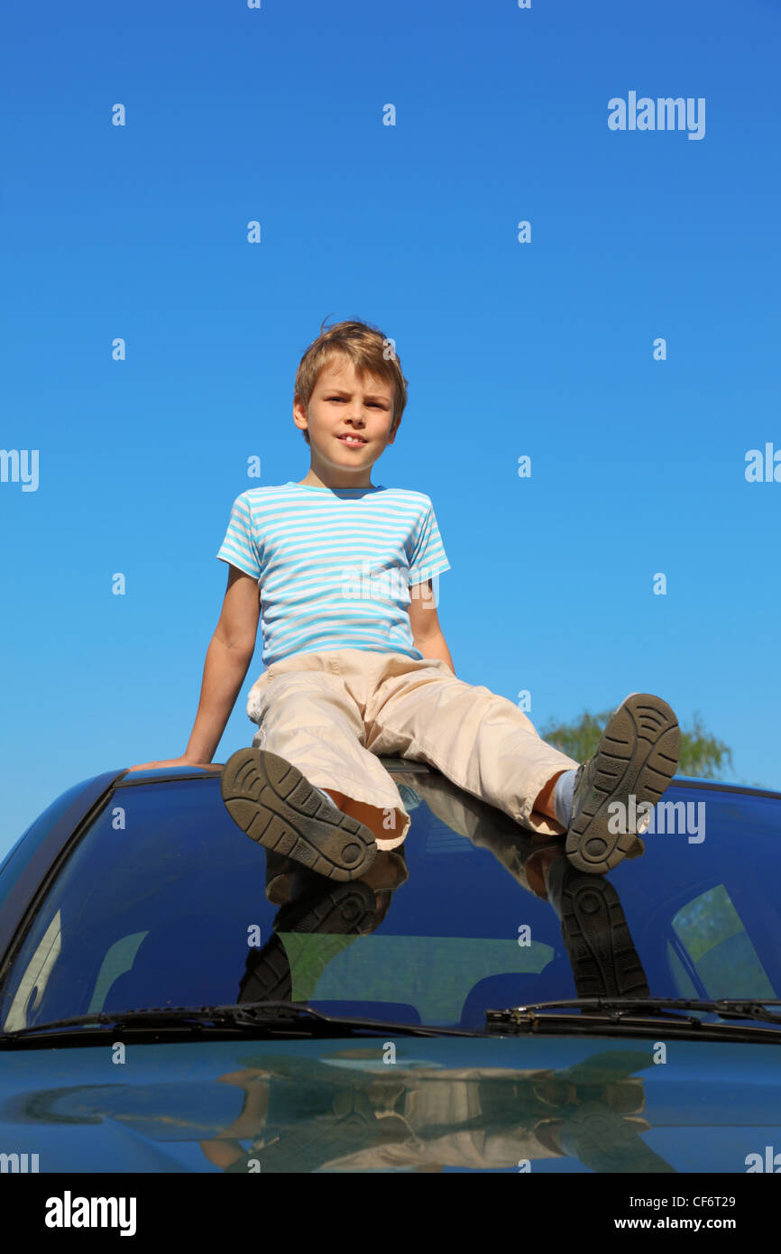 boy sitting on roof of car, blue sky Stock Photo