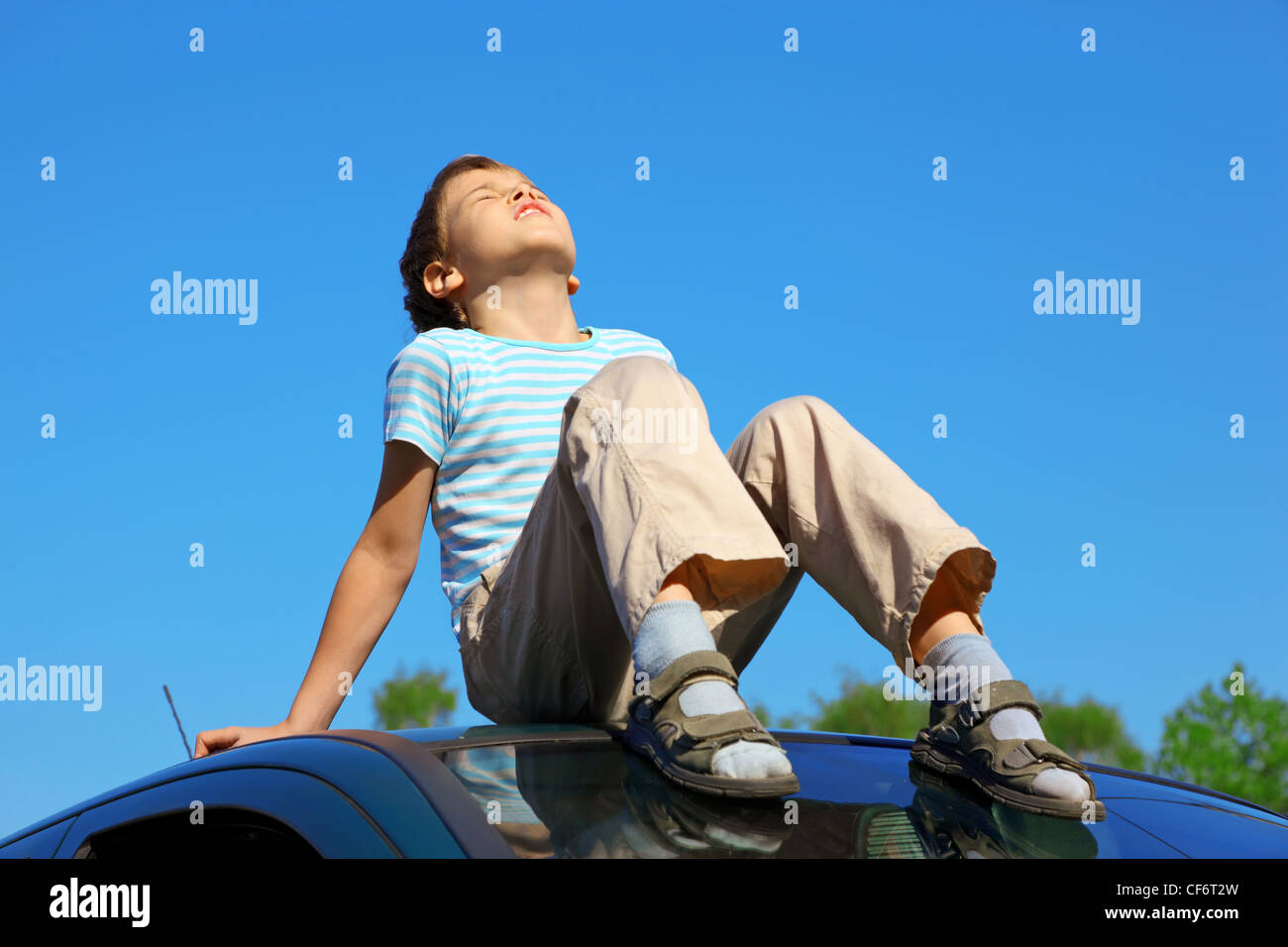 little boy with closed eyes sitting on car roof on blue sky Stock Photo ...