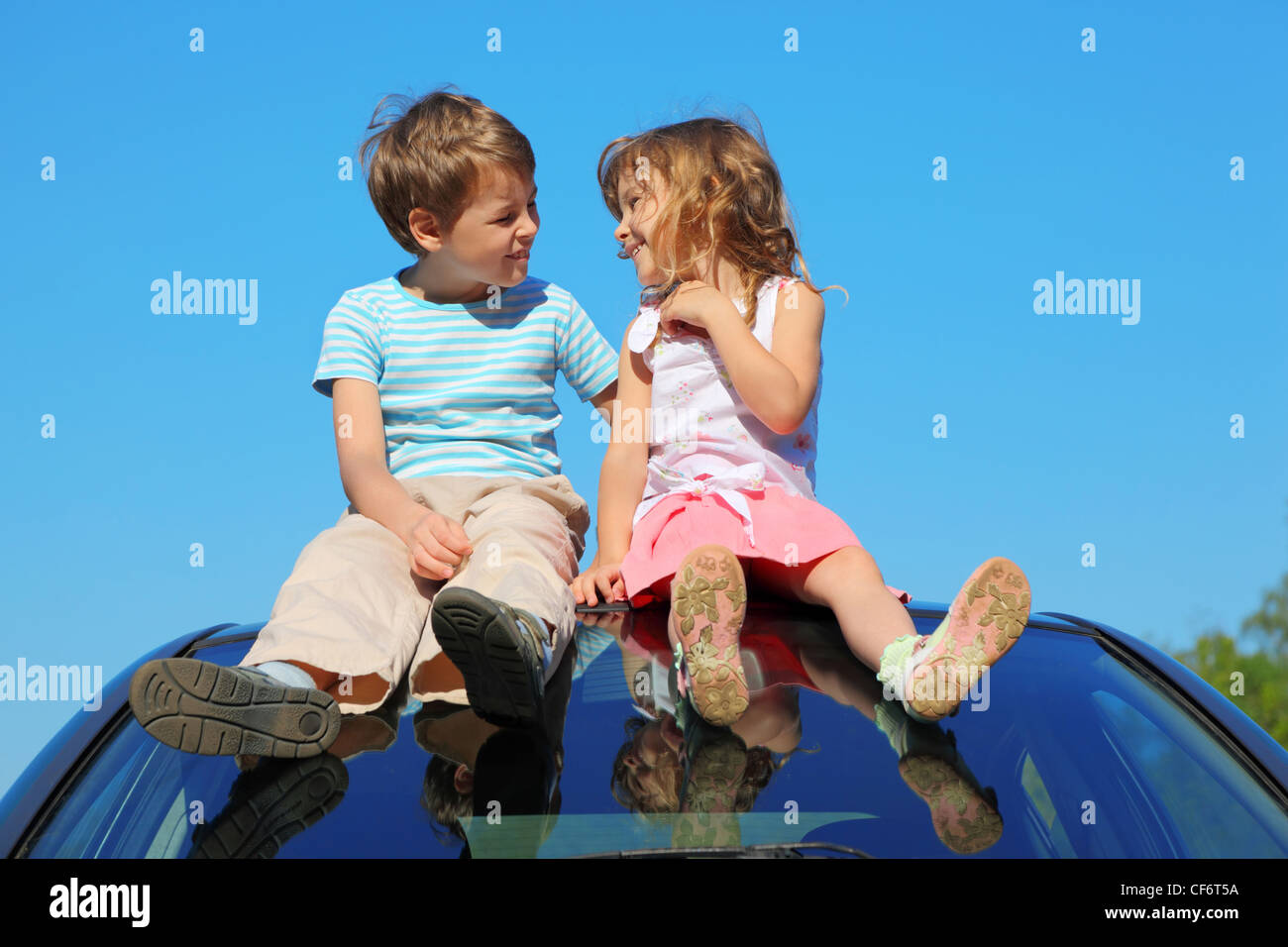 little boy and girl sitting on car roof on blue sky, talking Stock ...