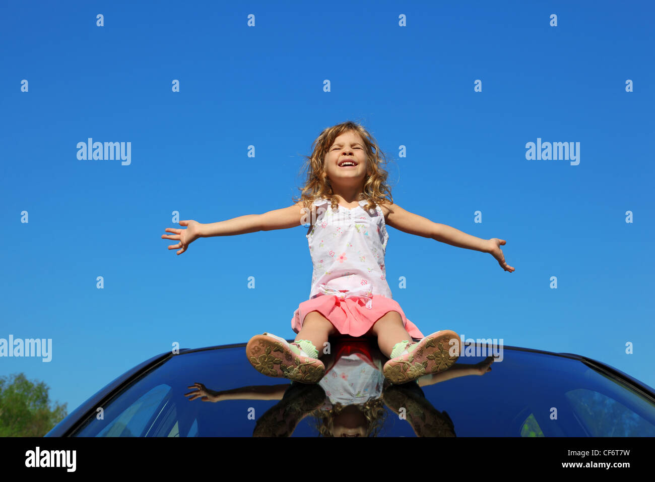 little girl sitting on car roof with open hands on blue sky Stock Photo ...