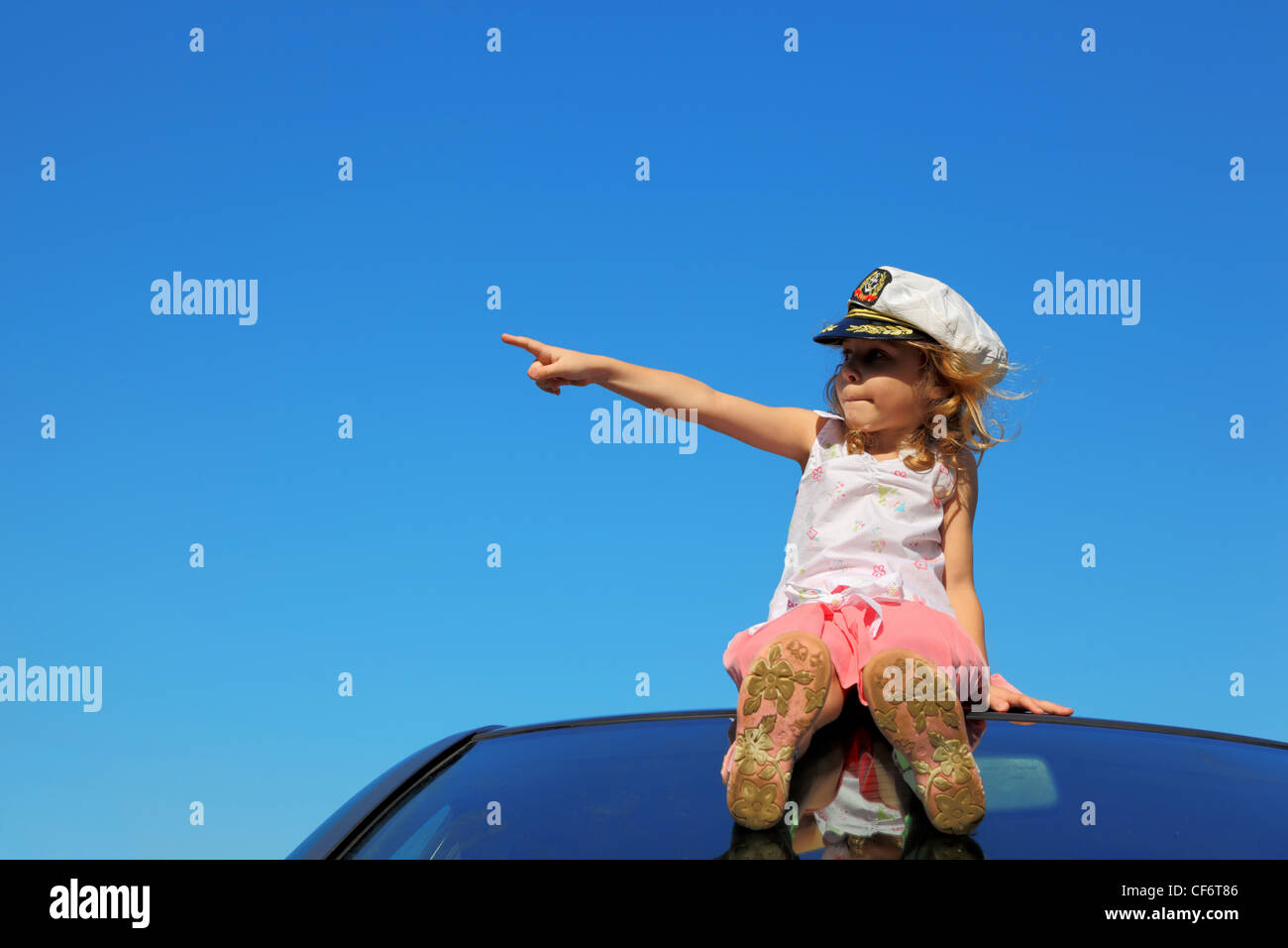 little girl sitting on car roof showing by finger on left side, blue ...