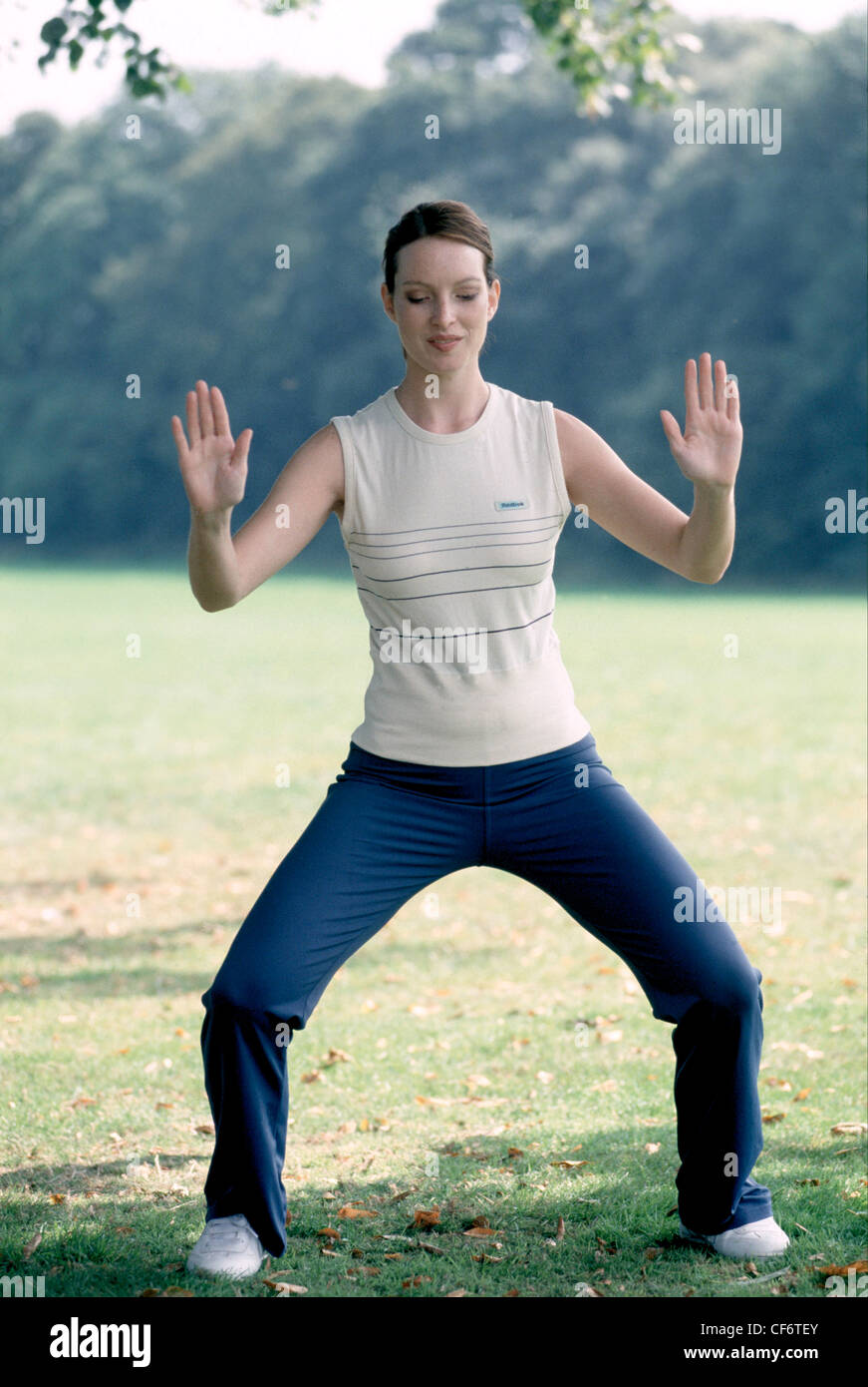 Semi profile of female short auburn hair in ponytail wearing cream vest top navy blue tracksuit bottoms and trainers, doing Stock Photo