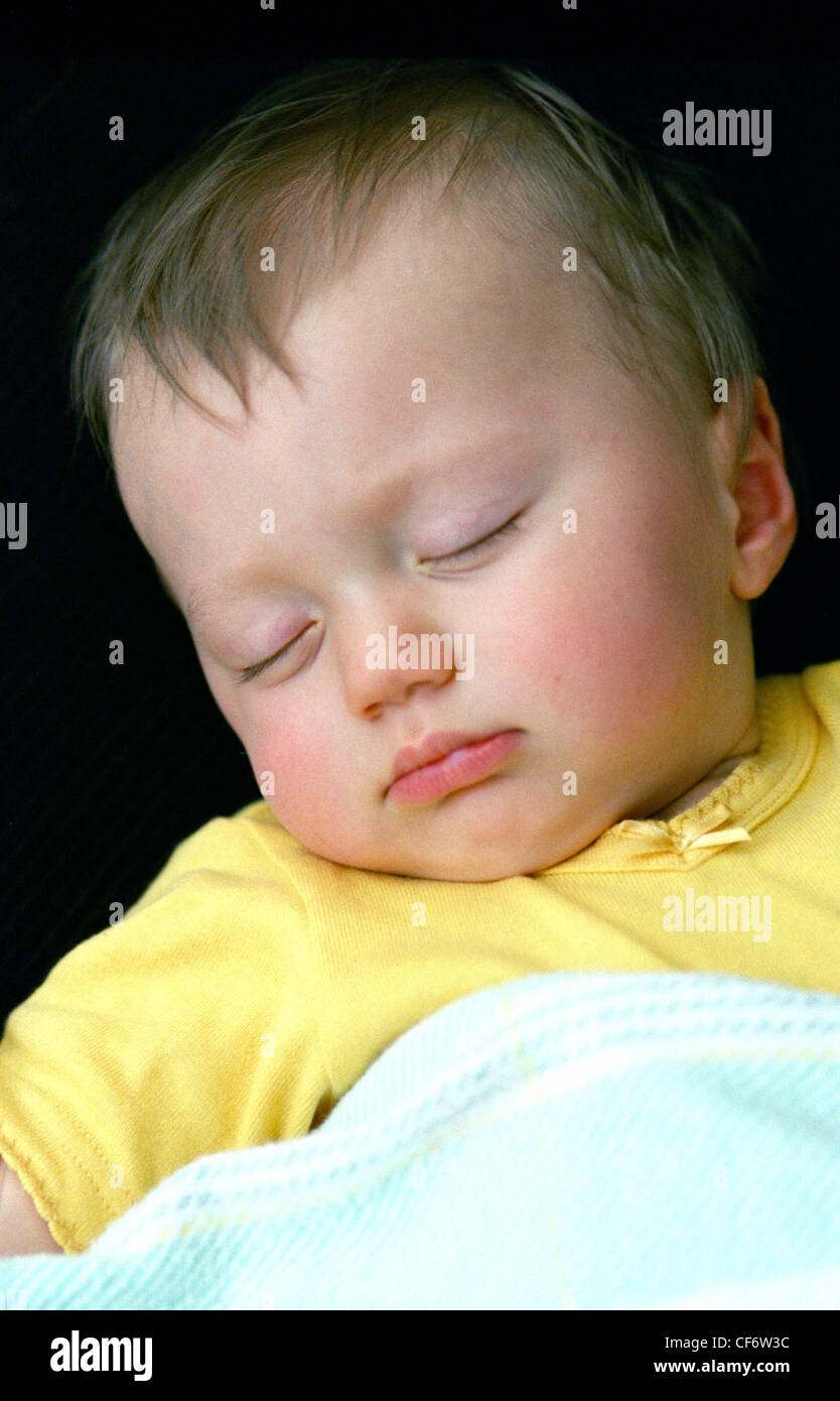 Female baby wearing yellow baby grow asleep on back head to one side