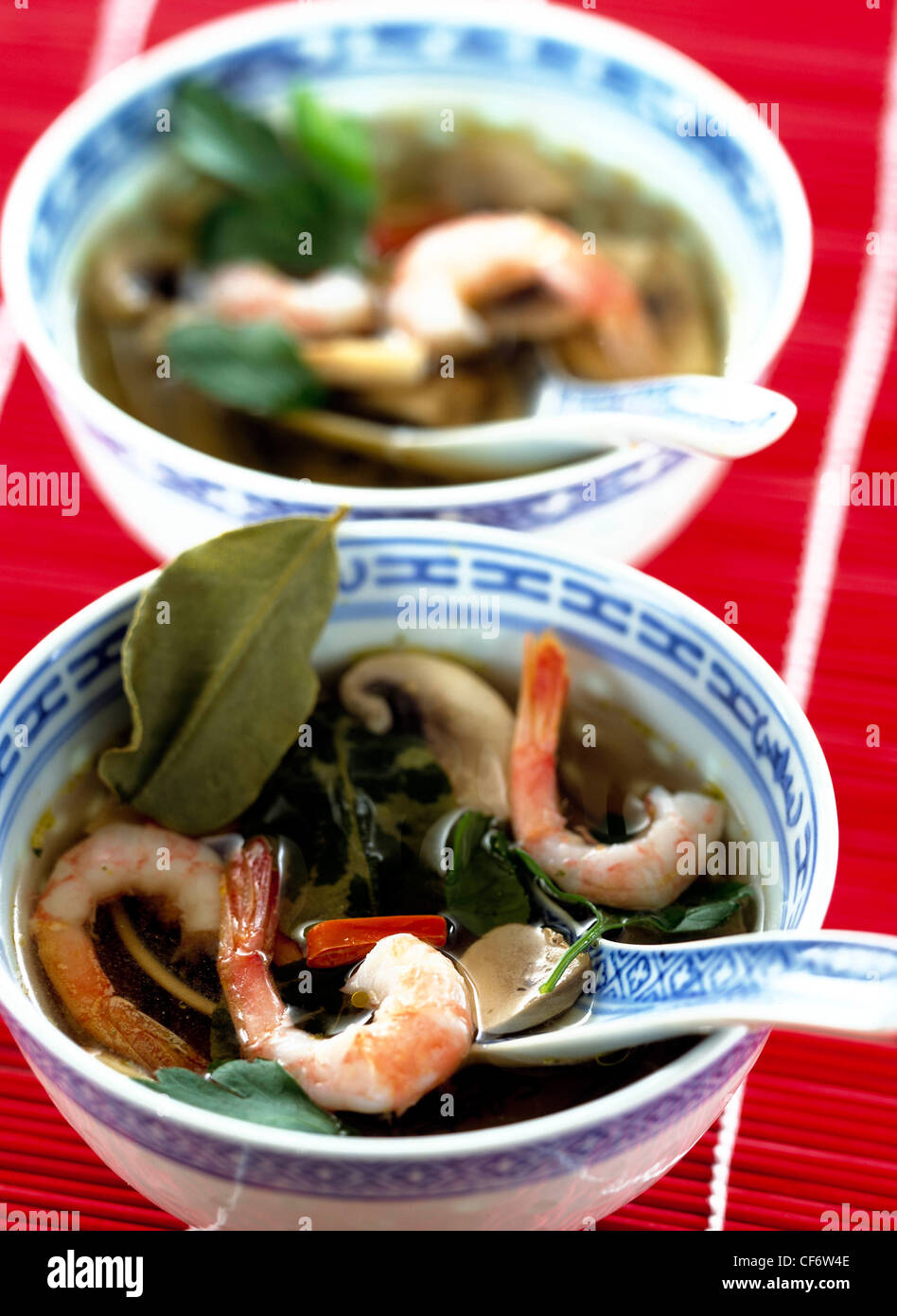 NOTwo blue and white china bowls matching spoons and spicy hot thai prawn soup lime leaves, chilli and mushroom on red and Stock Photo