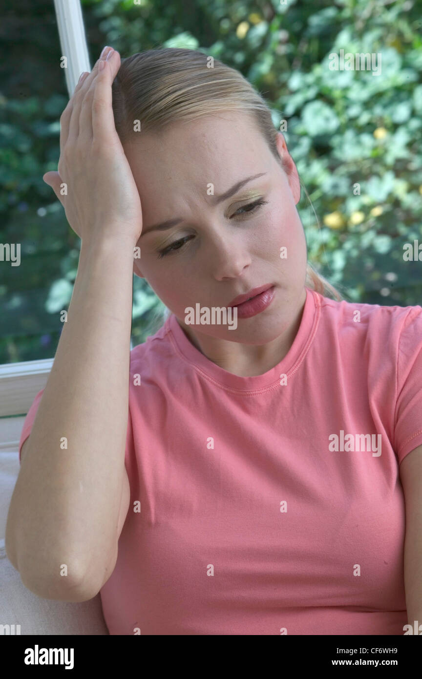 Female blonde hair off face wearing pink t shirt sitting on white sofa