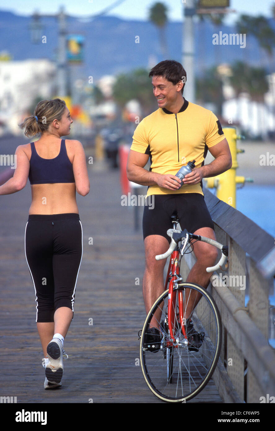 Male and female exercising passing each other going in opposite directions looking at each other smiling on wood decking by Stock Photo