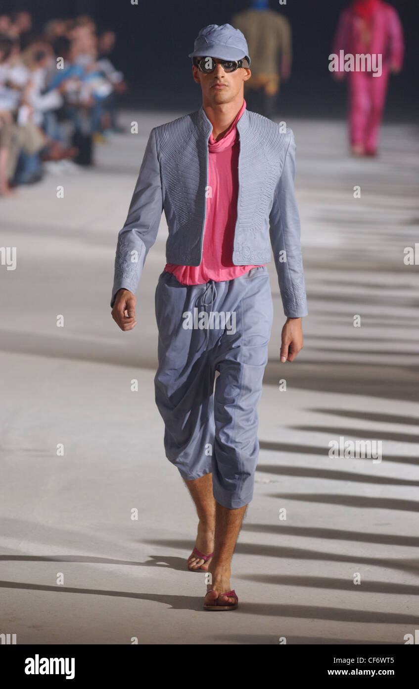 McQueen Menswear Ready to Wear Spring Summer Model wearing grey hat, flying goggles, pink shirt, grey fitted jacket, grey Stock Photo