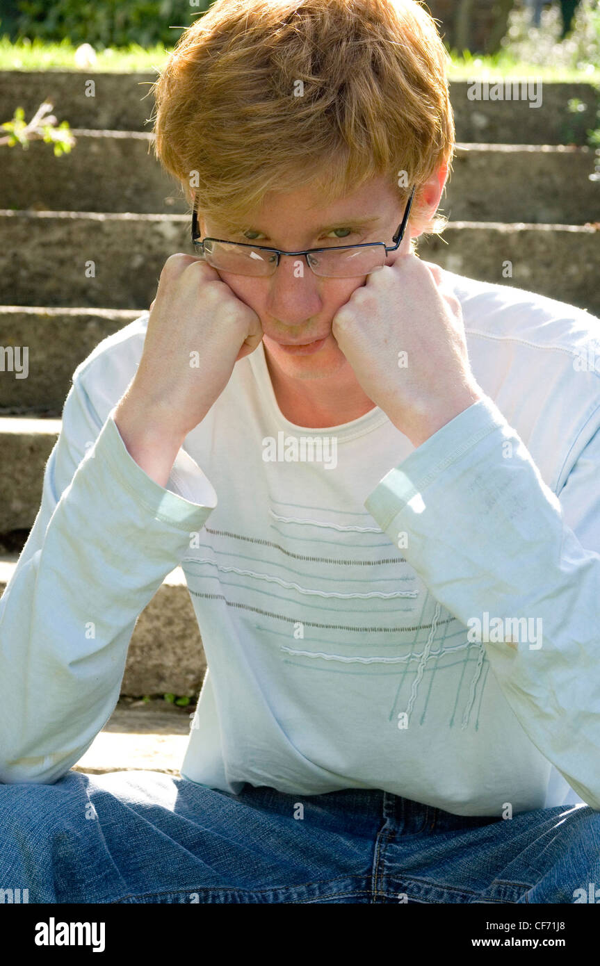 Male teenager sitting on steps with elbows on knees, fists clenched