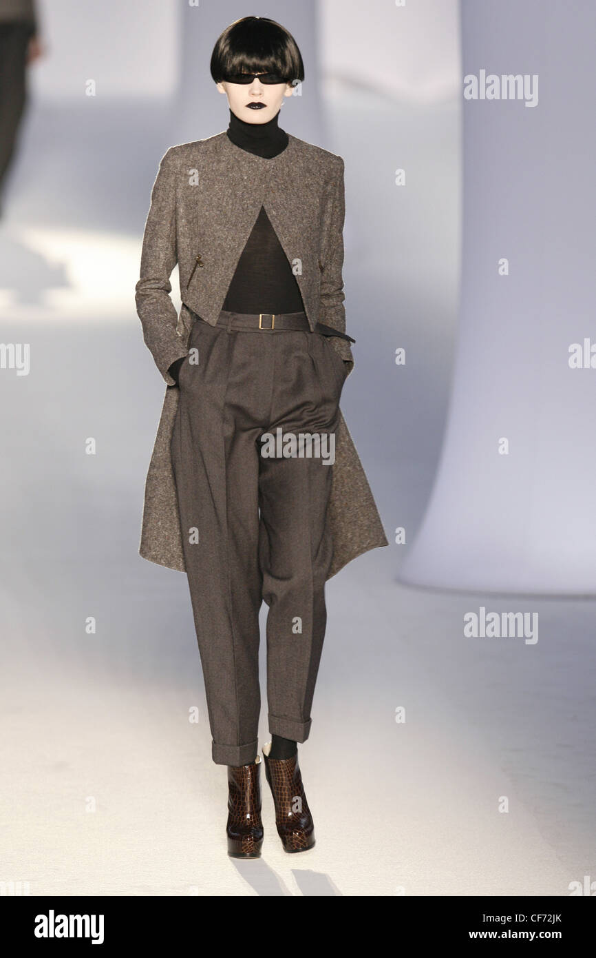 Model wearing grey cropped trousers, grey tweed frock coat and a black polo neck Stock Photo