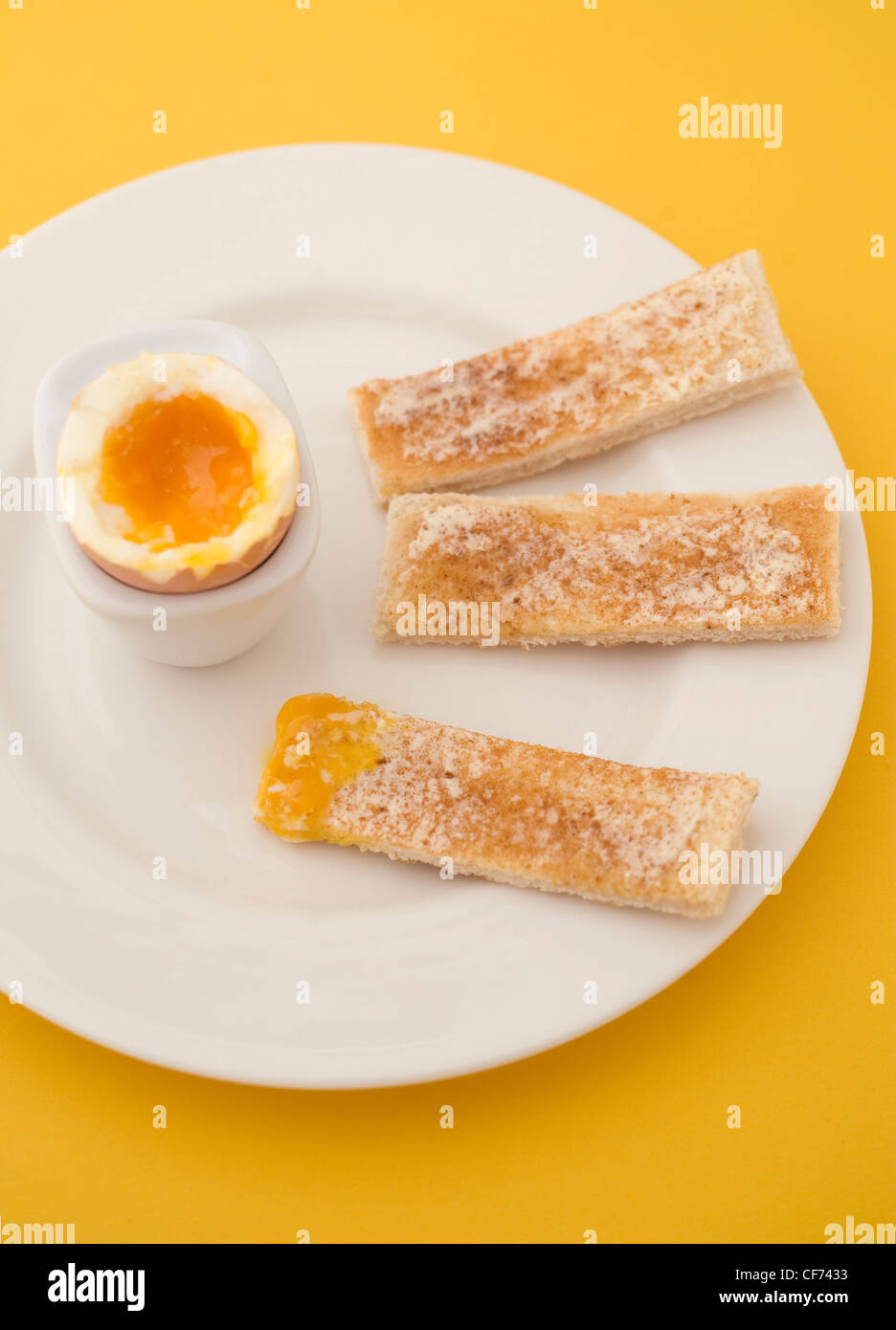 Soft boiled egg in a white egg cup on white plate with brown buttered toast fingers dipped in egg yolk Stock Photo