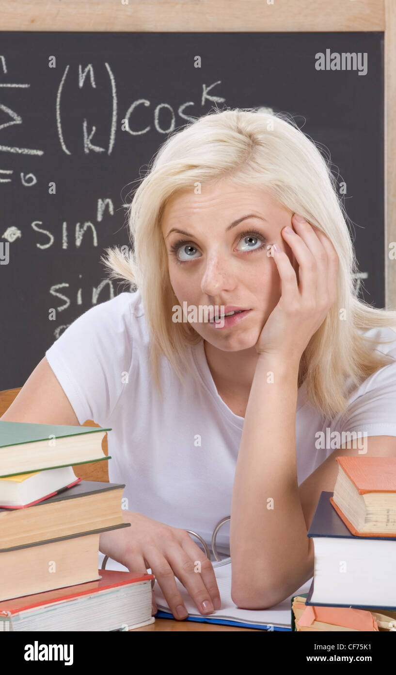Stressed High school or college female student by desk at math class. Blackboard with complicated advanced mathematical formulas Stock Photo