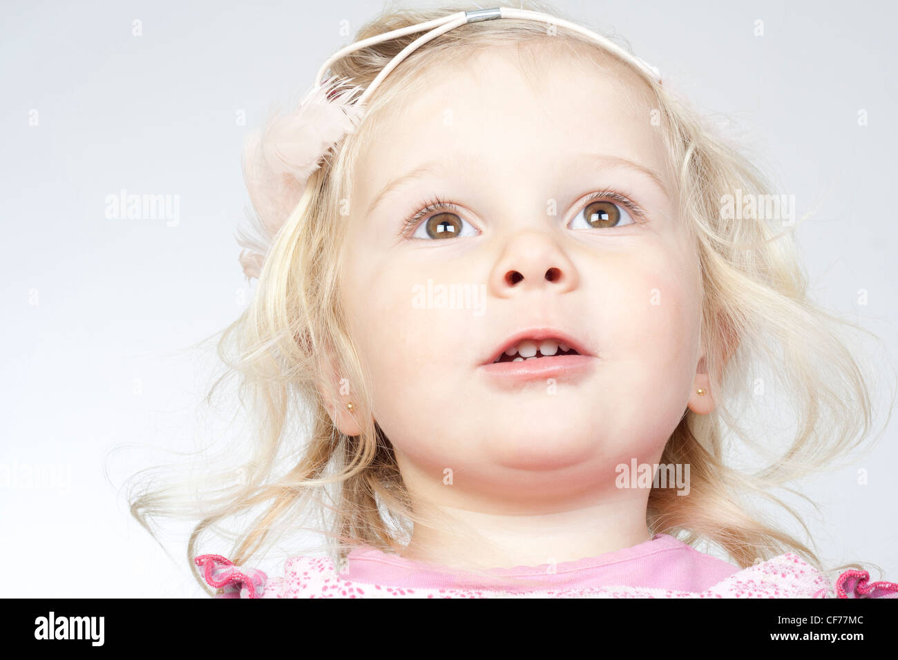 A beautiful blond baby girl looking up with expectation, dressing a pink hair band Stock Photo