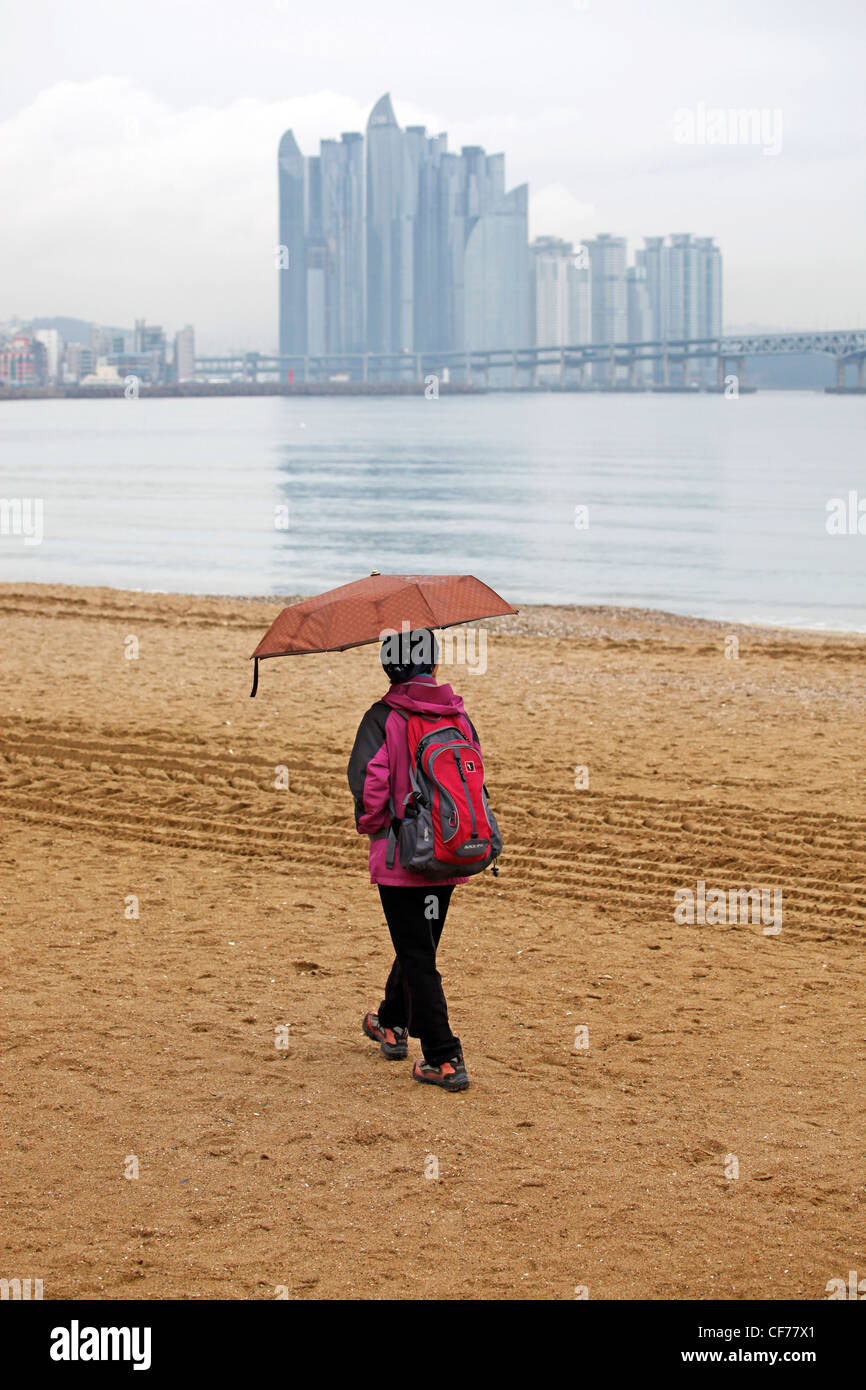 People walking along Gwangalli Beach with Machunroo on Dongbaek Island in the background in Busan, South Korea Stock Photo