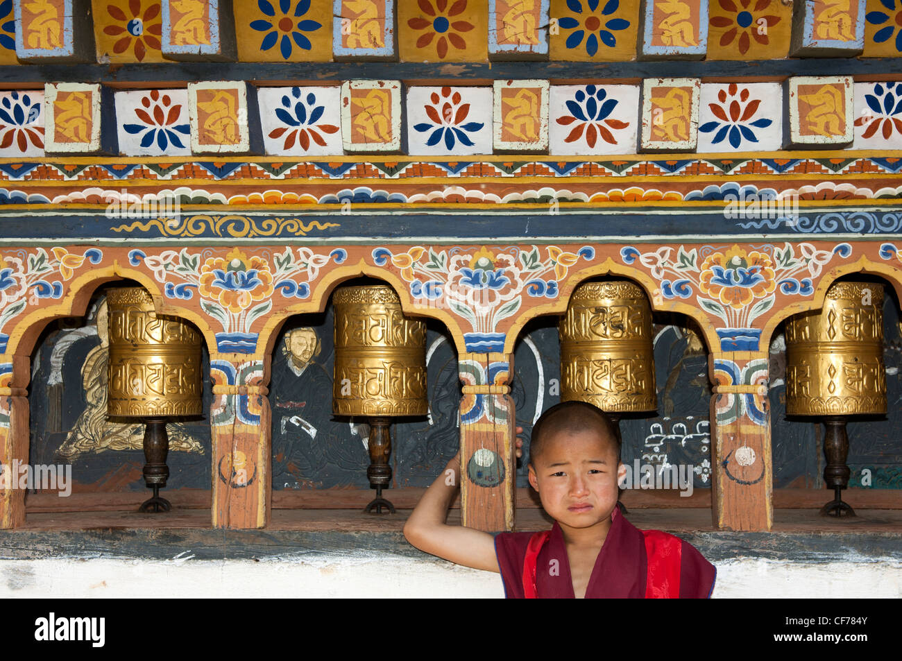 Infantile Buddhist monk standing by the prayer mills in the Temple of Fertility Chimi Lhakhang, Lobesa, Bhutan Stock Photo