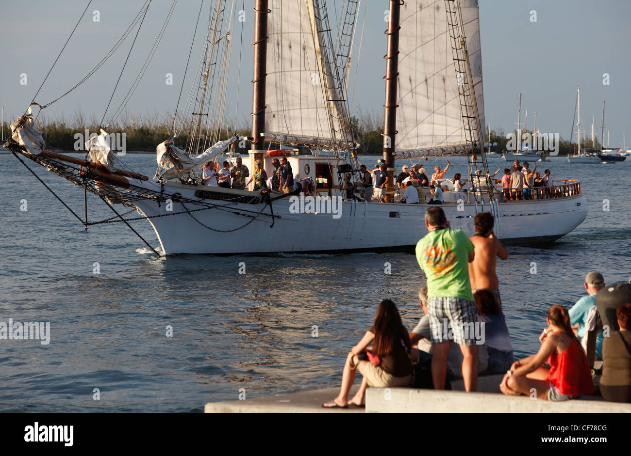 A sunset cruise boat passes people at Mallory Square, Key West, Florida Stock Photo