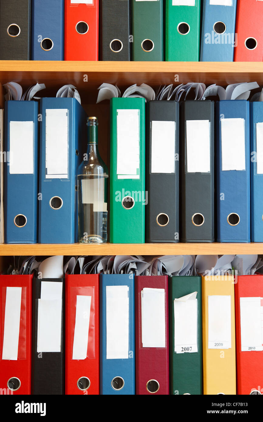 Glass bottle with alcohol hidden between file binders on shelves Stock Photo